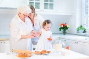 Happy Young Woman Baking A Cake With Her Senior Mother And Cute Little Toddler Daughter In A Beautif